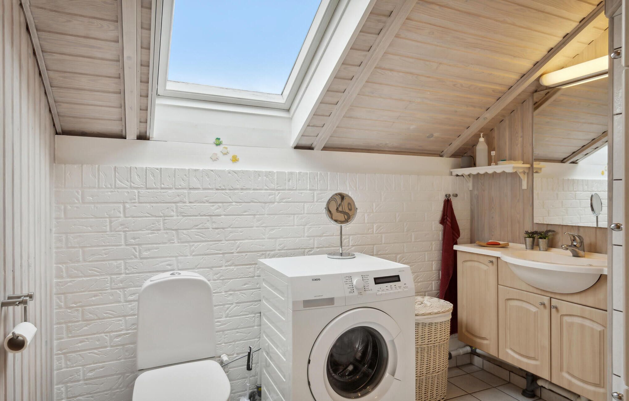 Een kleine, moderne badkamer met dakraam, een wasmachine, toilet en een wastafel met spiegel.