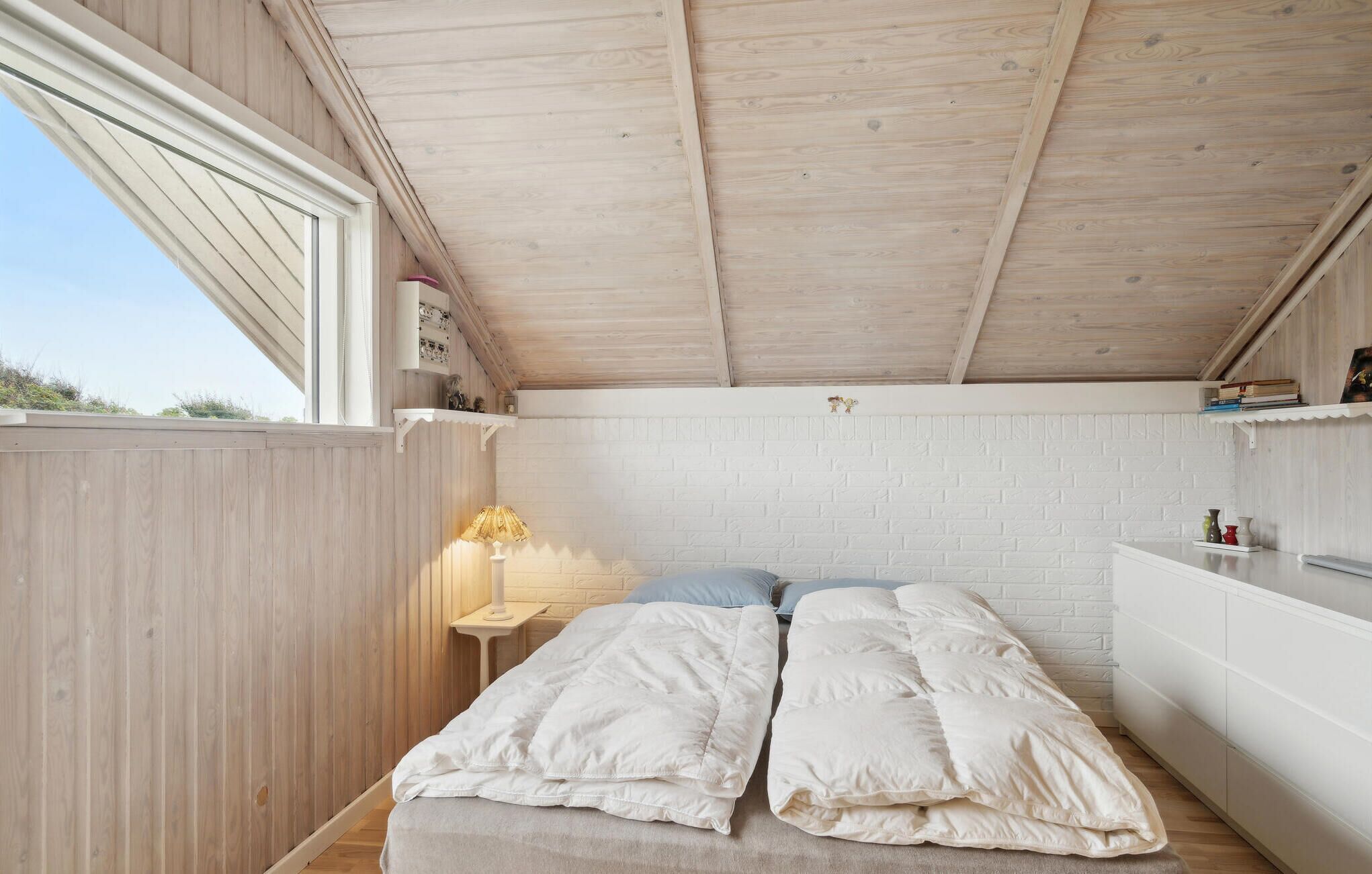 Une chambre avec un plafond en bois, un mur en briques blanches et un lit recouvert de linge de lit blanc.