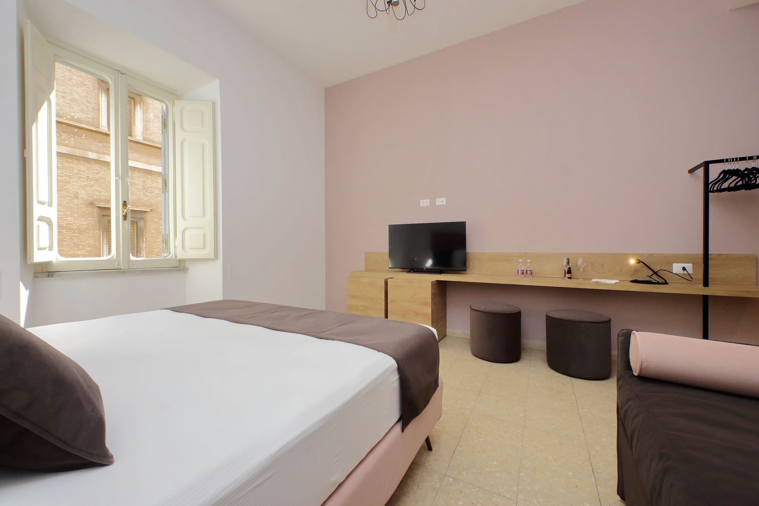 Quarto de hotel com uma cama, televisão, secretária de madeira e janela com persianas.
