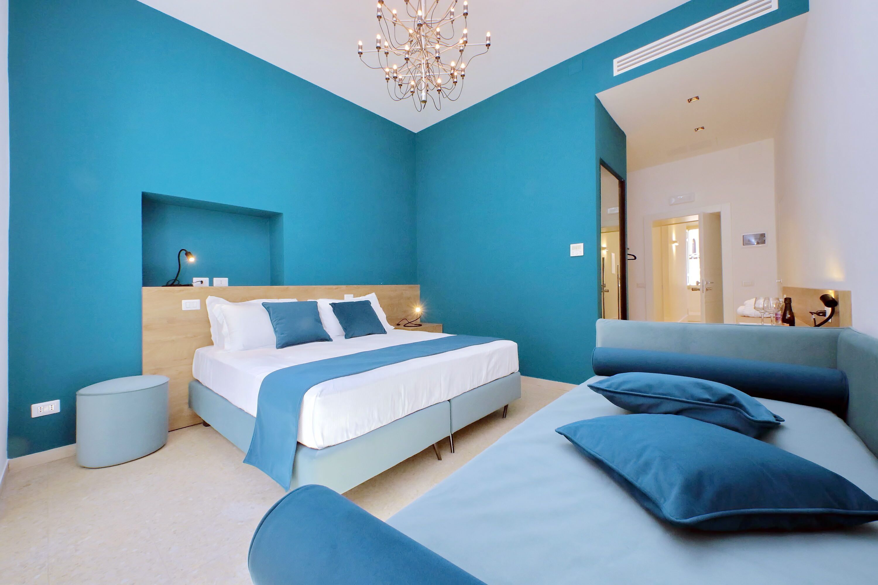 A modern bedroom with a bed, bedside tables, a round ottoman, and a large mirror.
