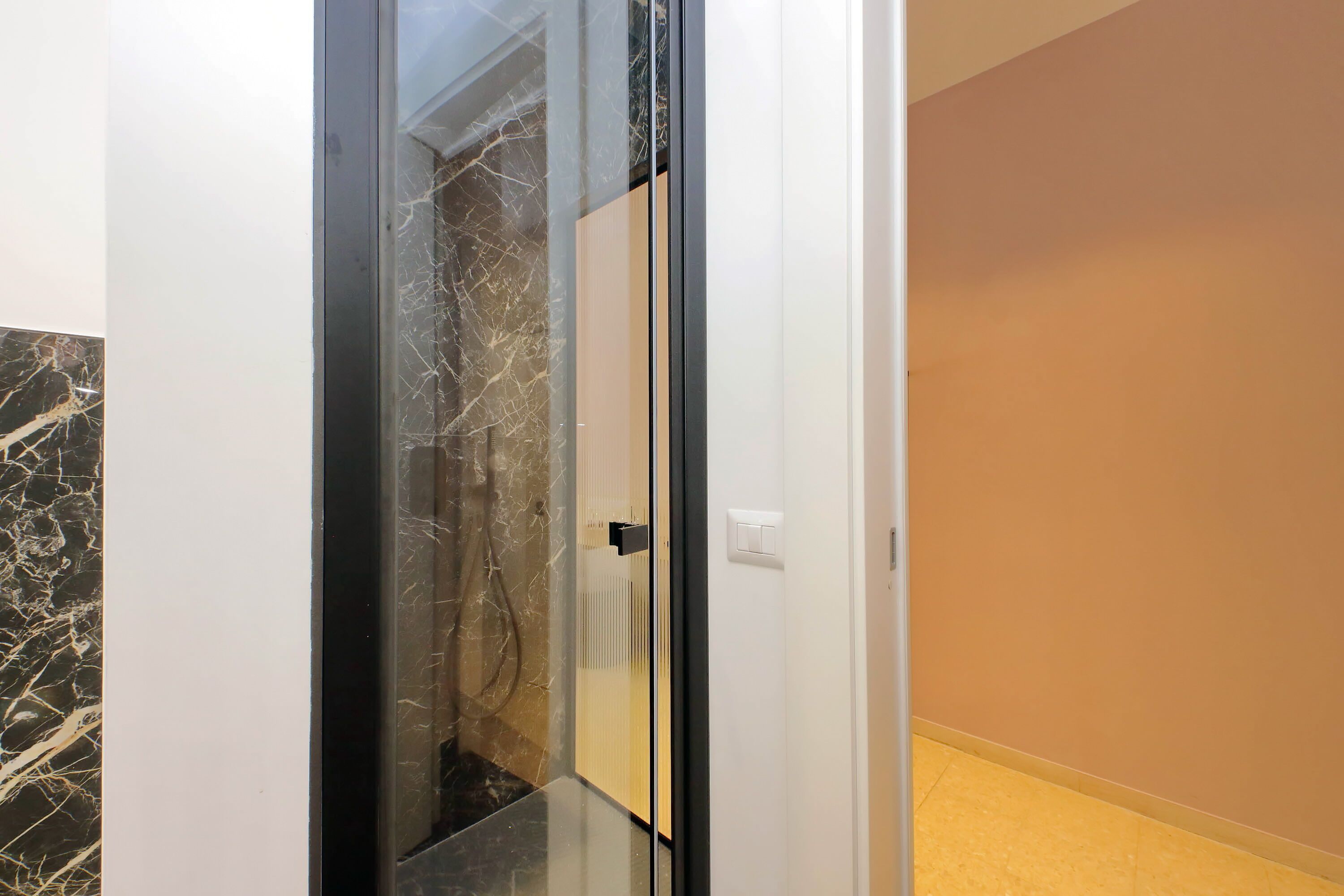 A modern interior with a glass elevator door, marble flooring, and a beige wall.