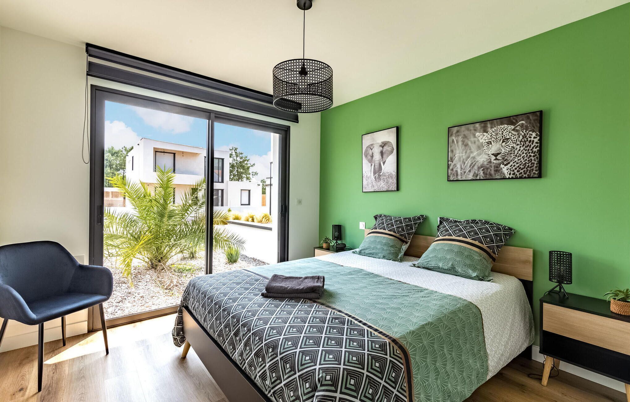 Une chambre moderne avec un grand lit, des murs verts et deux œuvres d’art murales sur le thème du léopard.