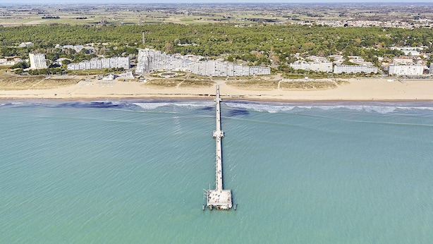 An aerial view of a coastal area with a long pier extending into the sea, surrounded by residential buildings and greenery. - Home with private pool (Saint-Jean-de-Monts)