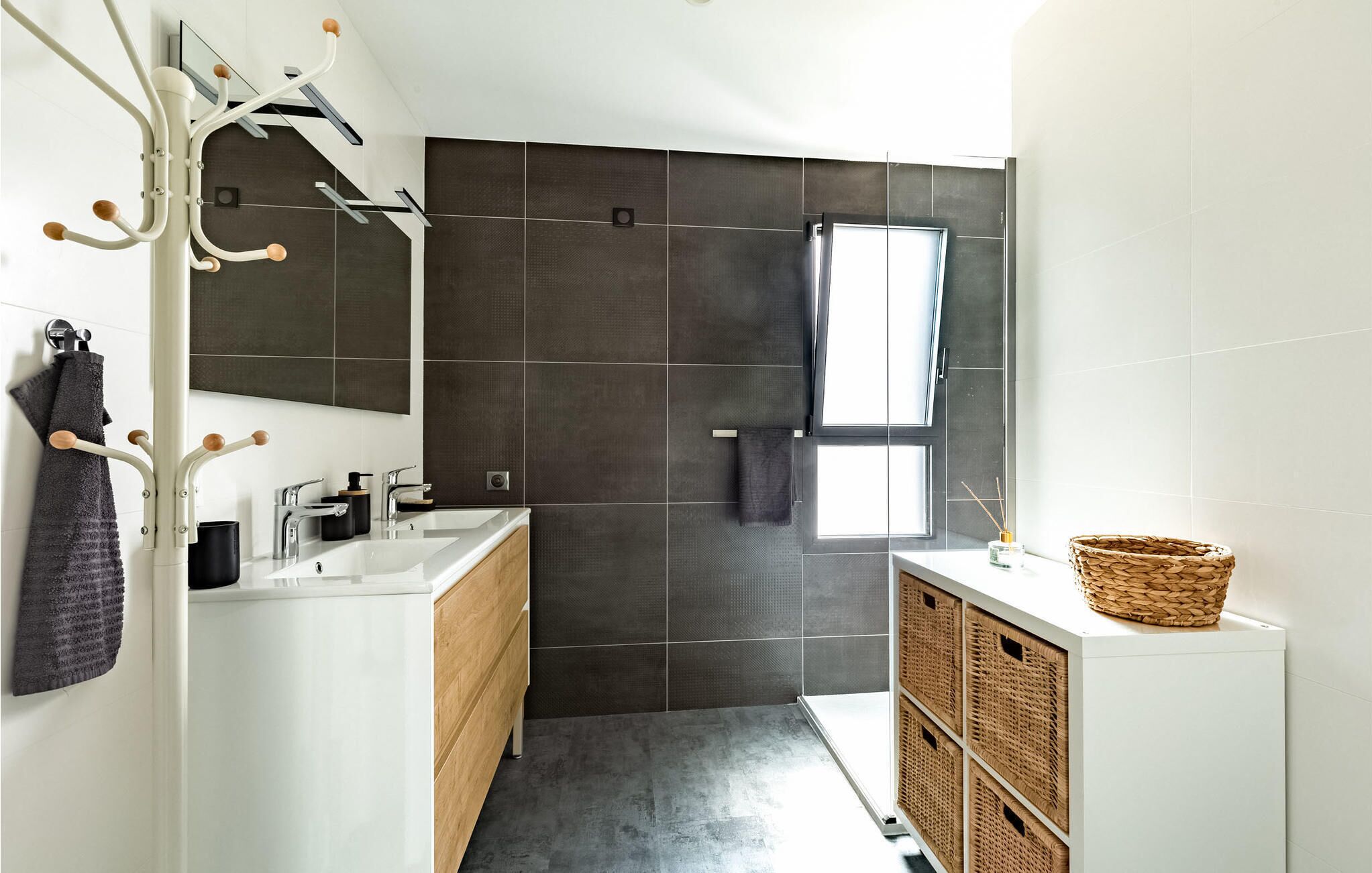 Ein modernes Badezimmer mit großem Spiegel, dunkel gefliesten Wänden, einem Fenster und einem weißen Waschbecken mit Holdekor.