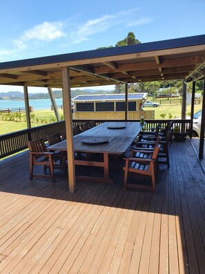 Una terraza de madera con una mesa y sillas, con vistas a un cuerpo de agua y colinas.