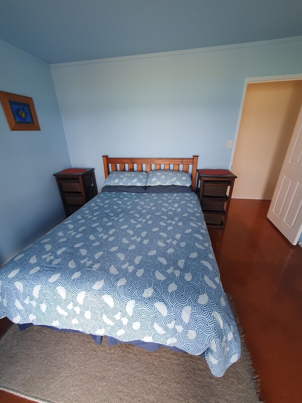 Un dormitorio con una cama, dos mesitas de noche, una puerta y un cuadro colgado en la pared.