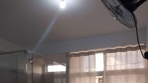 A room with a glass partition, a sliding glass door, a fan, a bed, and a table. - Hospedaje Moralillos (Yurimaguas)