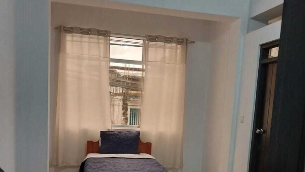 A room with two beds, a window with curtains, and a door. - Hospedaje Moralillos (Yurimaguas)