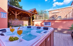 A hot tub with a glass of orange juice and a glass of wine, surrounded by a wooden deck and a brick wall. - Pet friendly home in Daruvar with sauna (Daruvar)