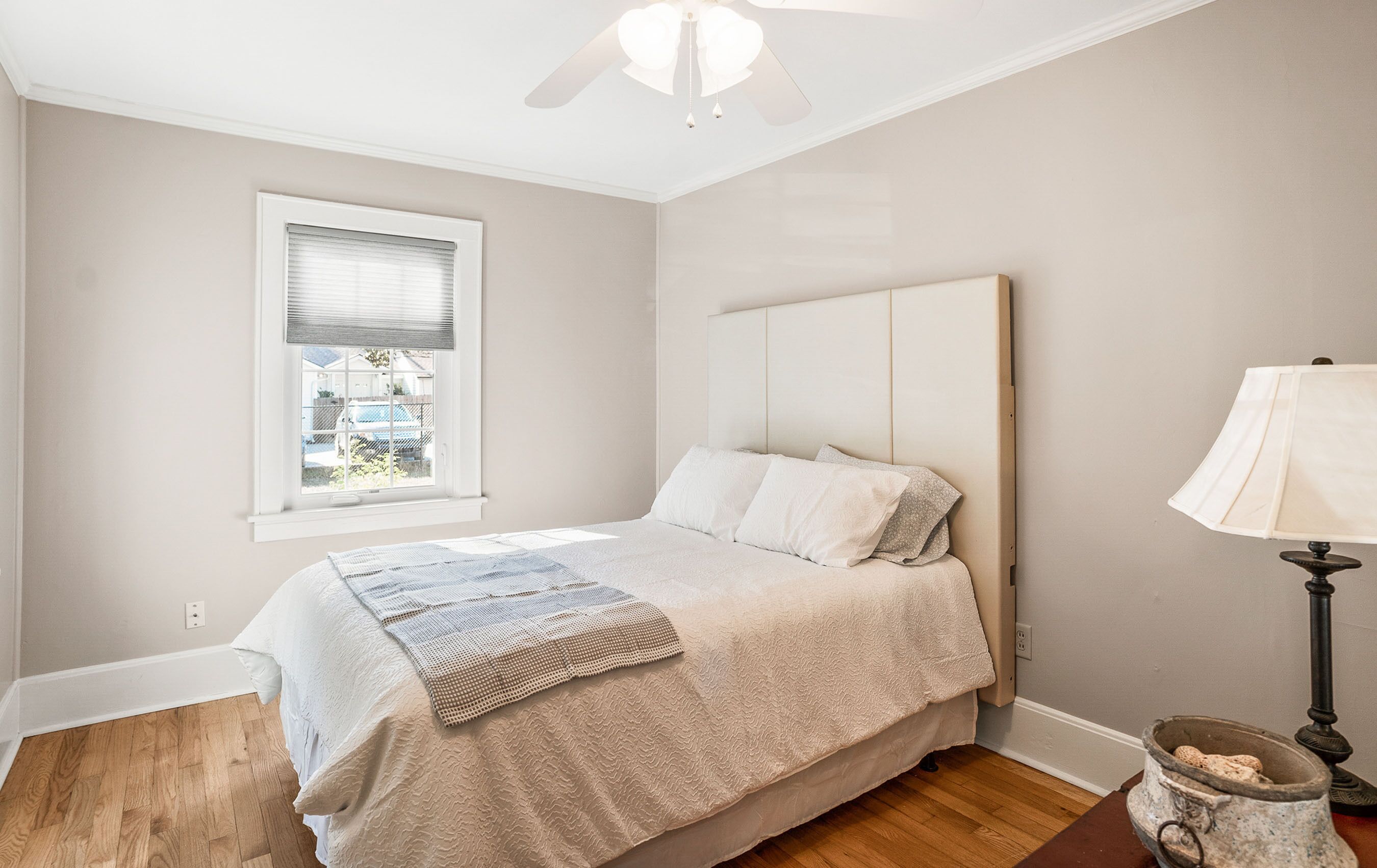 A bedroom with a bed, a window, a ceiling fan, and a lamp.