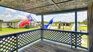 A covered porch with a lattice railing, a view of a grassy area, and a house in the background. - Deck & Fenced-In Yard: Texas Escape! (Freeport)