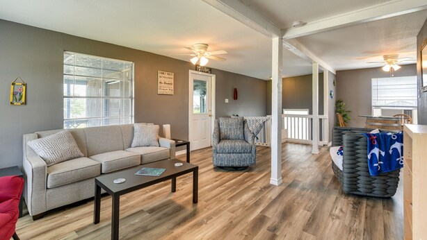 A spacious living room with a sofa, armchair, and coffee table. There is a ceiling fan, a door, and a window with blinds. - Deck & Fenced-In Yard: Texas Escape! (Freeport)