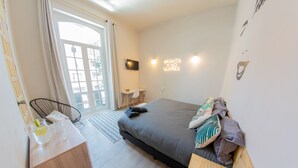 Ein modernes Schlafzimmer mit einem großen Bett, einem kleinen Schreibtisch, einem Stuhl und einem Fenster mit Vorhängen.