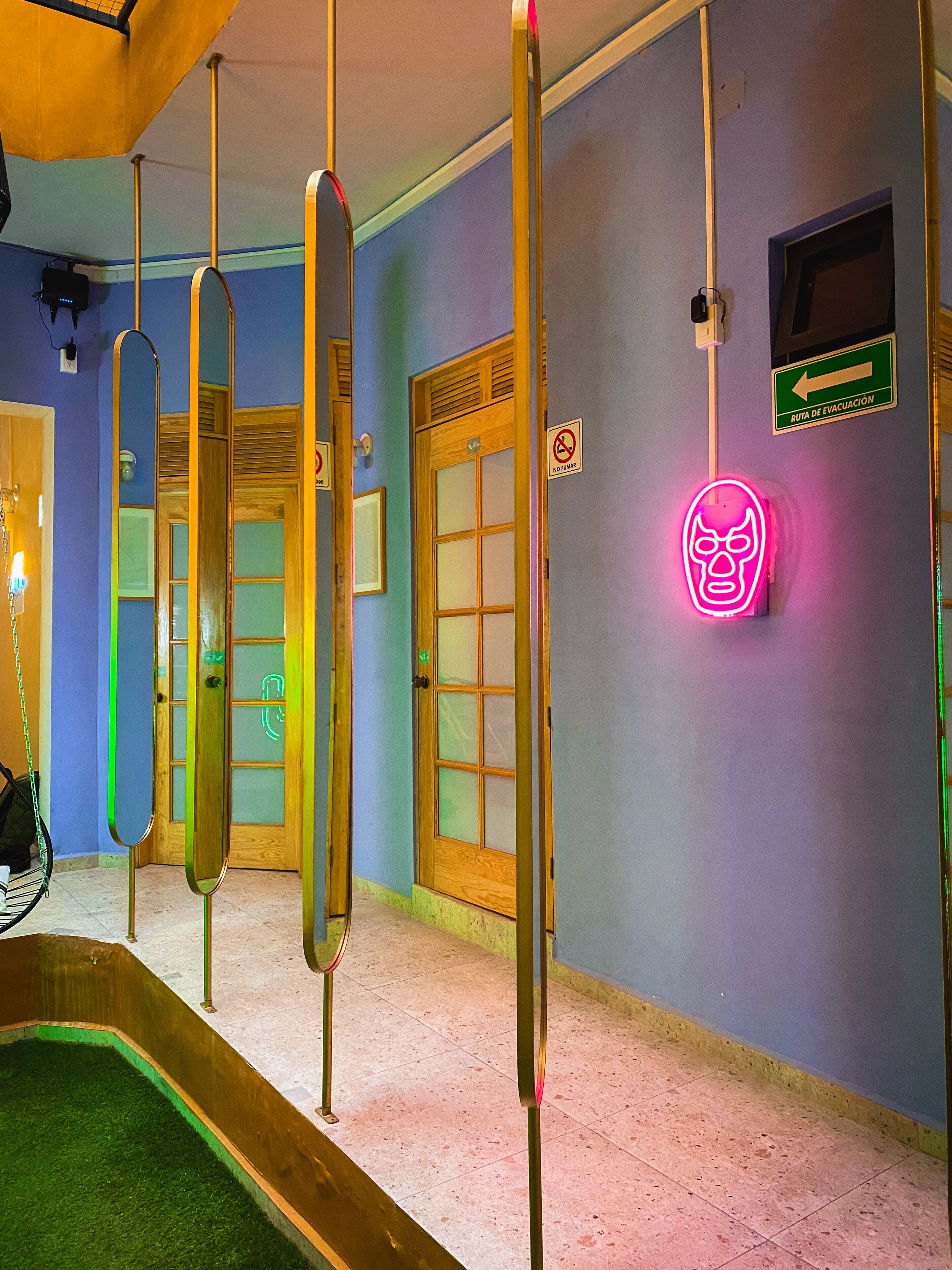 Un corridoio con porte di legno, un cartello a neon a forma di teschio e un segnale per vie di fuga verdi.