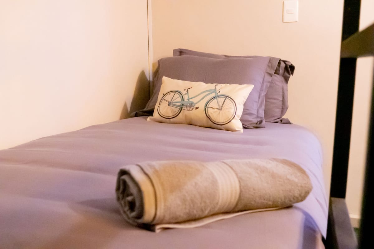Ein Bett mit einer zusammengerollten Decke, einem Kissen mit Fahrradmuster und zwei weiteren Kissen.