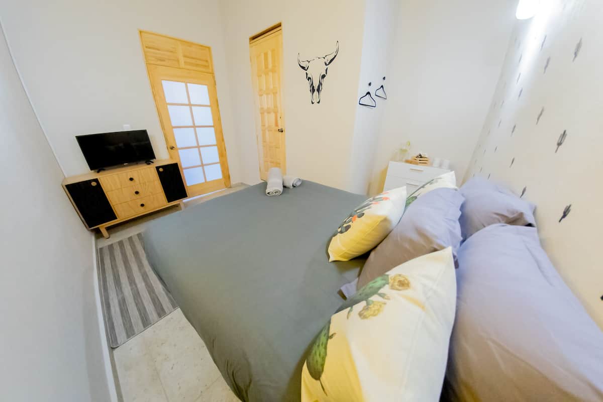 Ein Schlafzimmer mit einem Bett, einem Fernseher auf einer Holzkommode, einer Tür und Wanddekorationen.