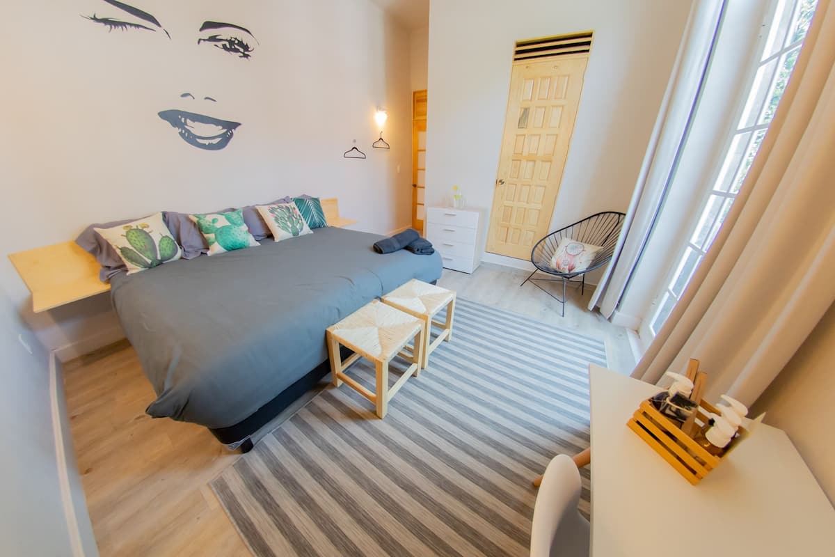 Ein Schlafzimmer mit Bett, Nachttischen, einem Sessel und einem Fenster.