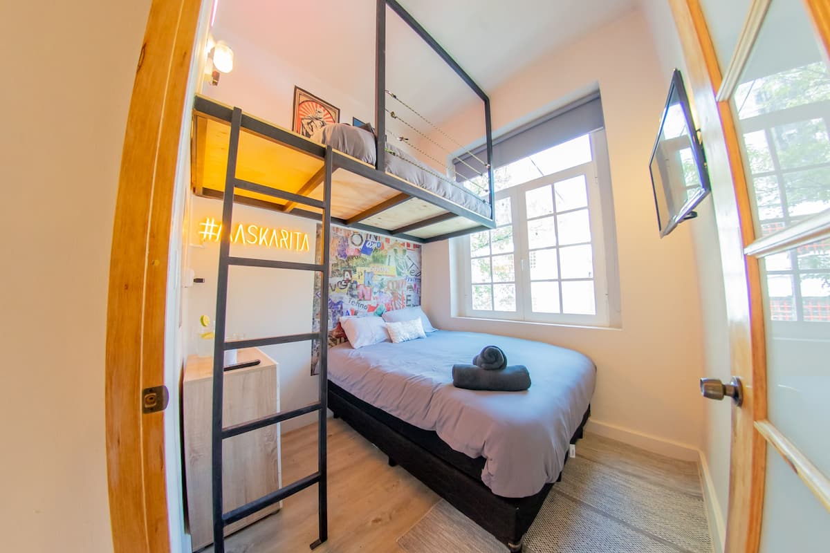 Ein Schlafzimmer mit Etagenbett, Schreibtisch, Fenster mit Aussicht und einer Wand mit einem farbenfrohen Wandbild.