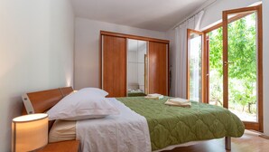 Un dormitorio con cama, lámpara de noche, armario y ventana con vistas a zonas verdes.