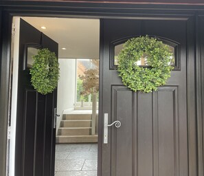 A dark wooden door with two green wreaths and a metal door handle.