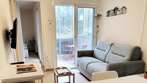 Un espacio habitable pequeño con sofá, una mesa, un taburete y un televisor sobre un mueble.
