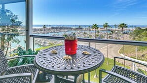 Un balcón con mesa y sillas, con vistas a un puerto deportivo y una playa.