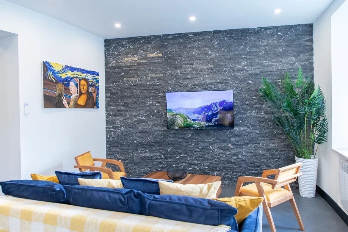 A modern living room with a stone wall, a flat-screen TV, a sofa with cushions, and a potted plant.