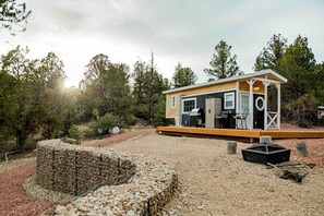 A compact cabin with a wooden deck, a small outdoor seating area, and a gravel ground.