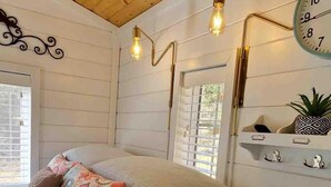 Un dormitorio acogedor con techo de madera, una cama con muchas almohadas, un reloj de pared y una estantería con objetos decorativos.