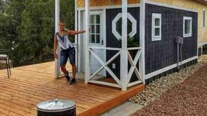 Una cabaña con terraza de madera, un porche con barandas blancas y un ventanal con diseño geométrico.