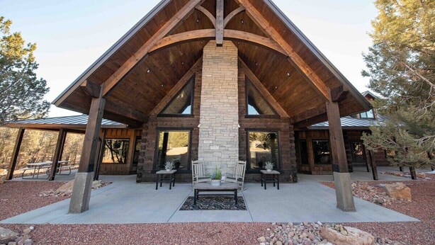 A modern lodge with a stone fireplace, wooden beams, and large windows. - New! Juniper Ridge Luxury Lodge @ East Zion & Bryce (Orderville)