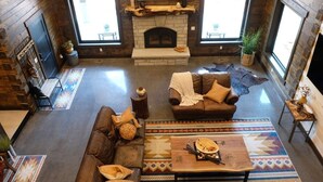 A spacious living room with a fireplace, leather sofas, and a large rug. - New! Juniper Ridge Luxury Lodge @ East Zion & Bryce (Orderville)