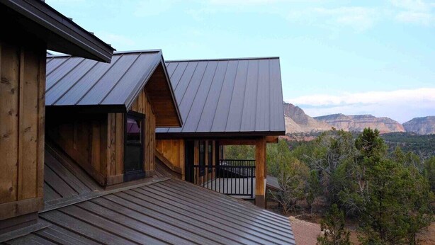 A wooden cabin with a metal roof, a balcony, and a view of mountains.