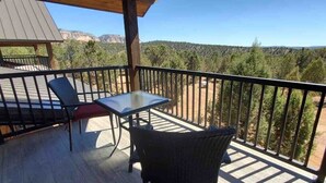 A balcony with a table and chairs, overlooking a forested landscape.