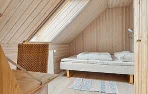 A small, wooden attic bedroom with a sloped ceiling, a bed with white bedding, a woven rug, and a wooden chair.