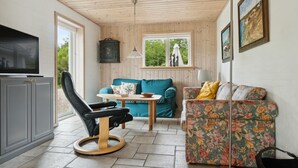 Een gezellige kamer met een houten plafond, een televisie op een kast, een blauwgroene bank, een bank met bloemenprint en een klein tafeltje met een schaal.