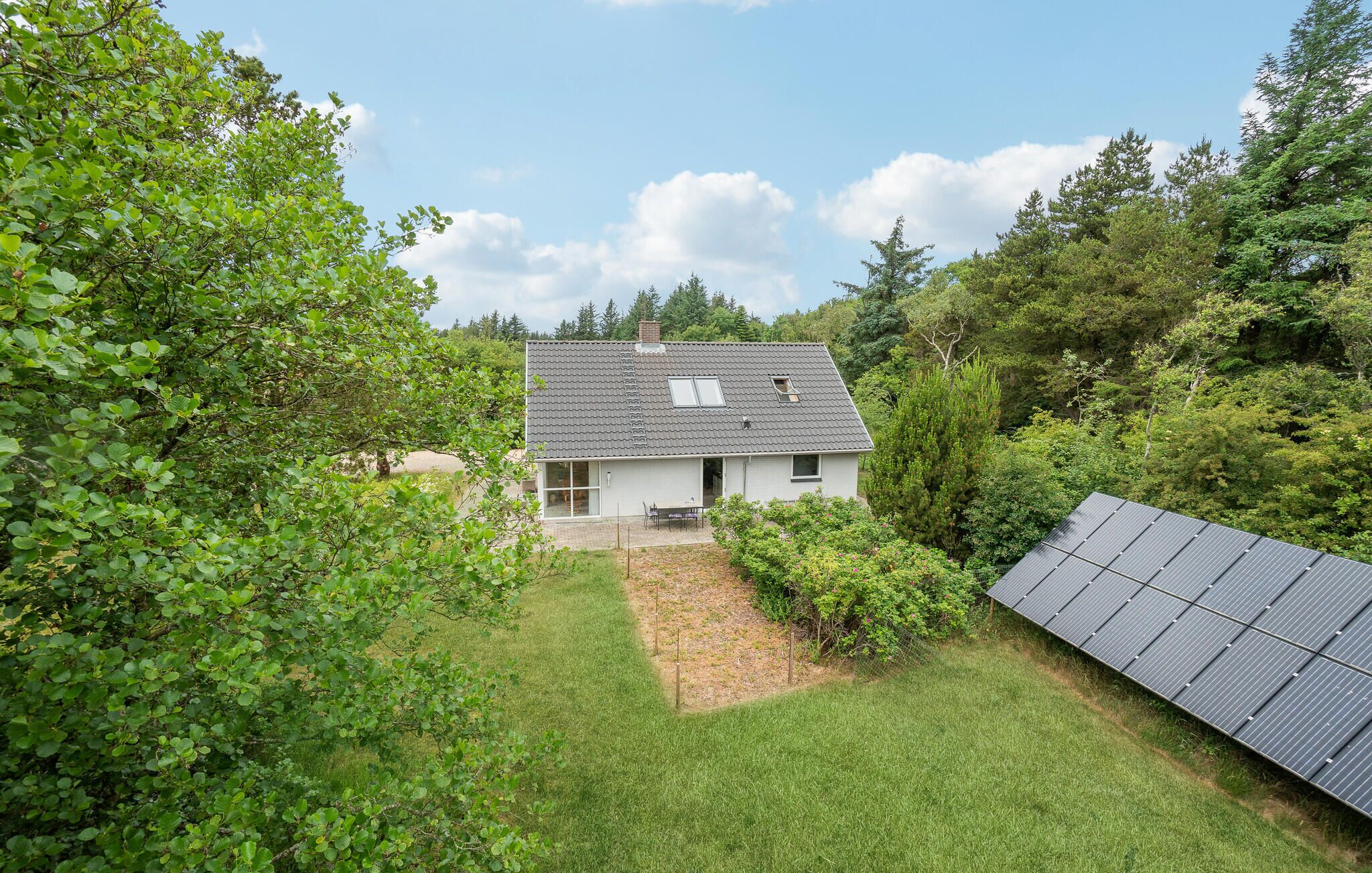 Uma casa com telhado inclinado, um pequeno jardim e painéis solares.