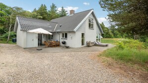 Een huis met twee verdiepingen, een grindpad, een overdekt terras met tuinmeubilair en een kleine schuur.