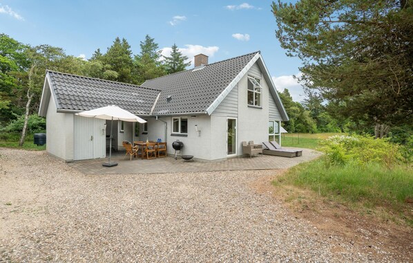 A two-story house with a gravel driveway, a covered patio with outdoor furniture, and a small shed.