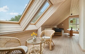 A cozy attic room with wooden floors, a glass table, wicker chairs, and a bed.