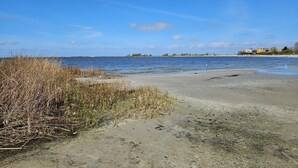A beach with clear water, a sandy shore, and a distant shoreline with buildings.