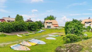 A coastal area with thatched-roof cottages, a grassy path, and windsurfing equipment.