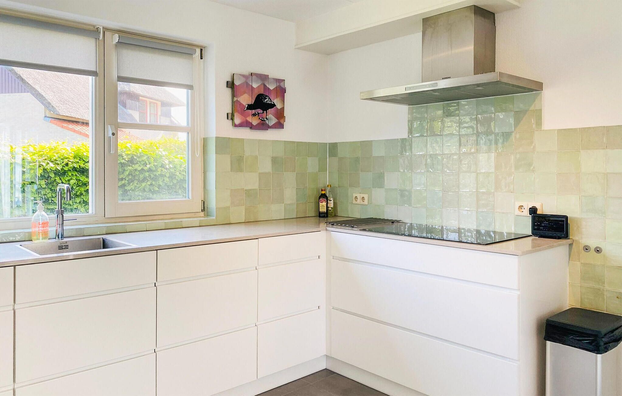 A modern kitchen with white cabinets, a stainless steel sink, a window, and a tiled backsplash.