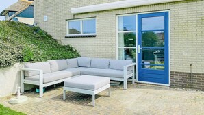 A modern outdoor seating area with a white sectional sofa and ottoman, a blue door, and a brick wall.