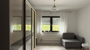 A modern bedroom with a large bed, a grey sofa, and a window with blinds. - Seerhein apartment (Konstanz)
