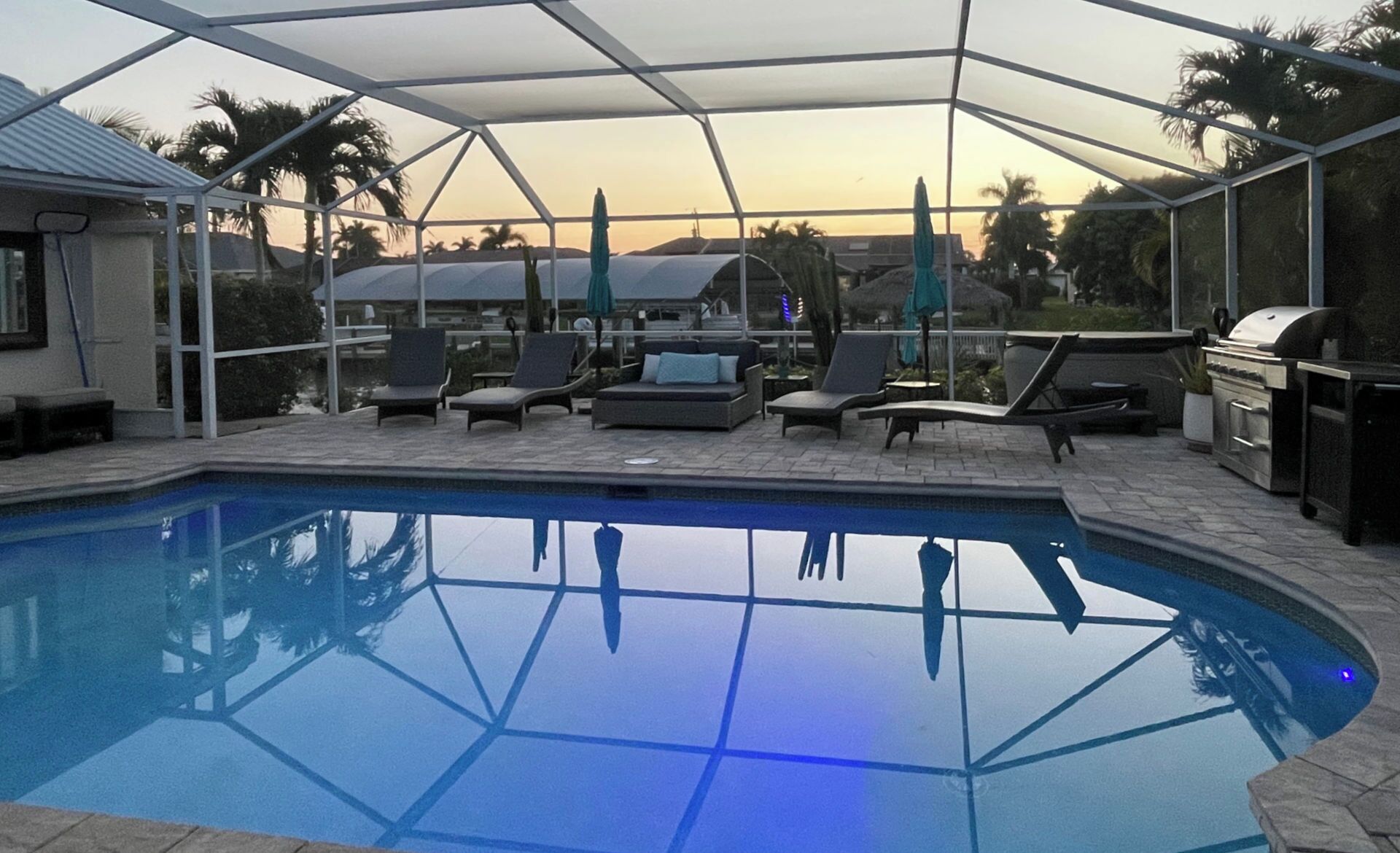 A covered outdoor pool area with lounge chairs and a barbecue grill.