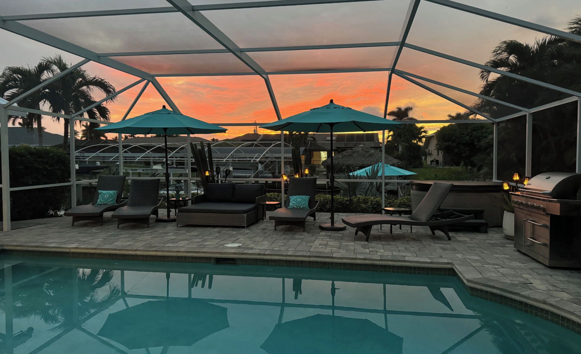 A covered outdoor seating area with lounge chairs and umbrellas, a barbecue grill, and a swimming pool.