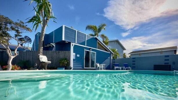 Ein modernes Haus mit Swimmingpool, Palmen und blauem Himmel.