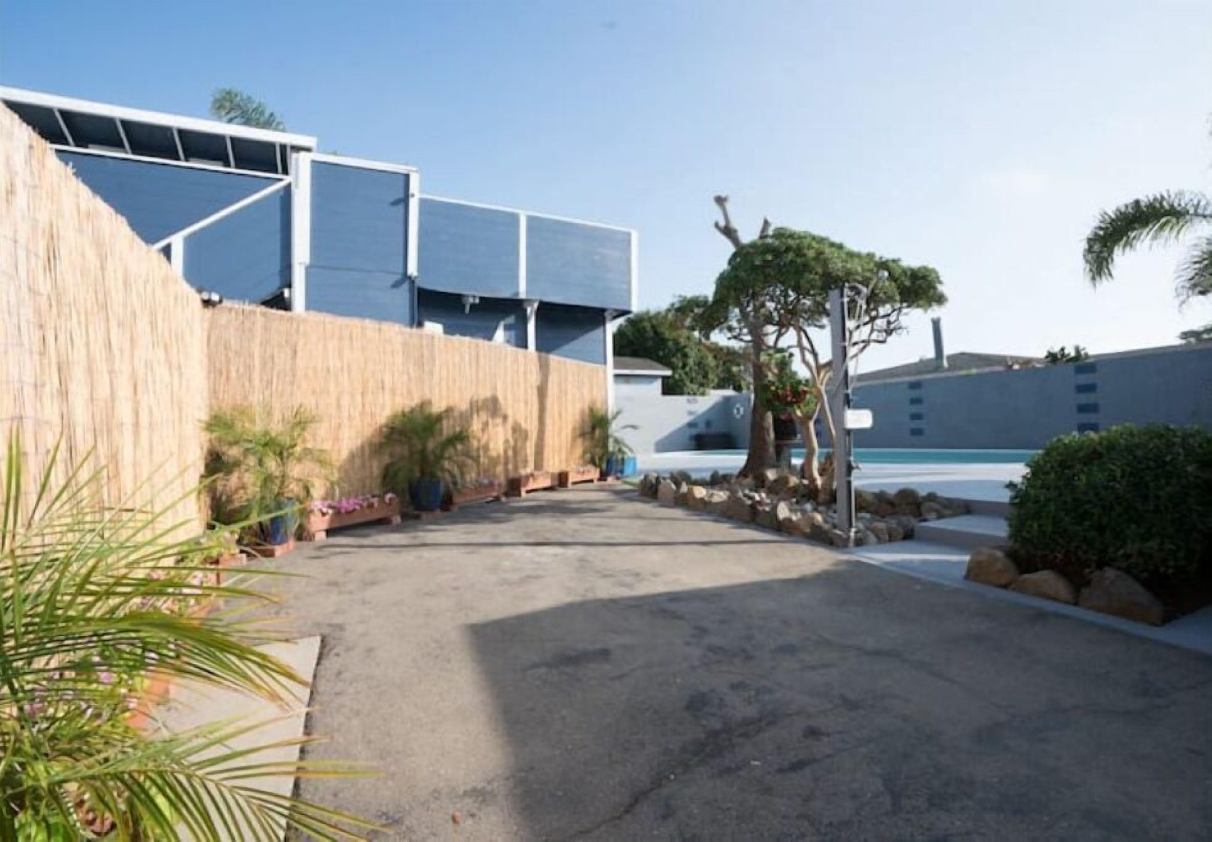 Un edificio moderno con techo plano, ventanas amplias y un patio empedrado con plantas y un árbol.