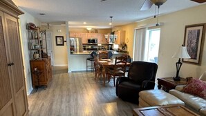 A spacious living room with a wooden coffee table, a leather sofa, and a dining area with wooden chairs and a table. - 2 bdr/2 bth Courtyard Villa in The Villages w/ Cart Lake Sumter Spanish Springs (The Villages)